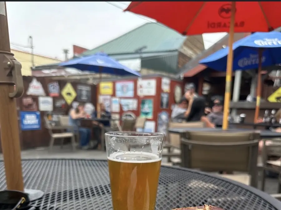 The Snag Bar's back patio: mesh tables under red and blue umbrellas, a wall of old beer signs behind them, and a pint on the table in the foreground.